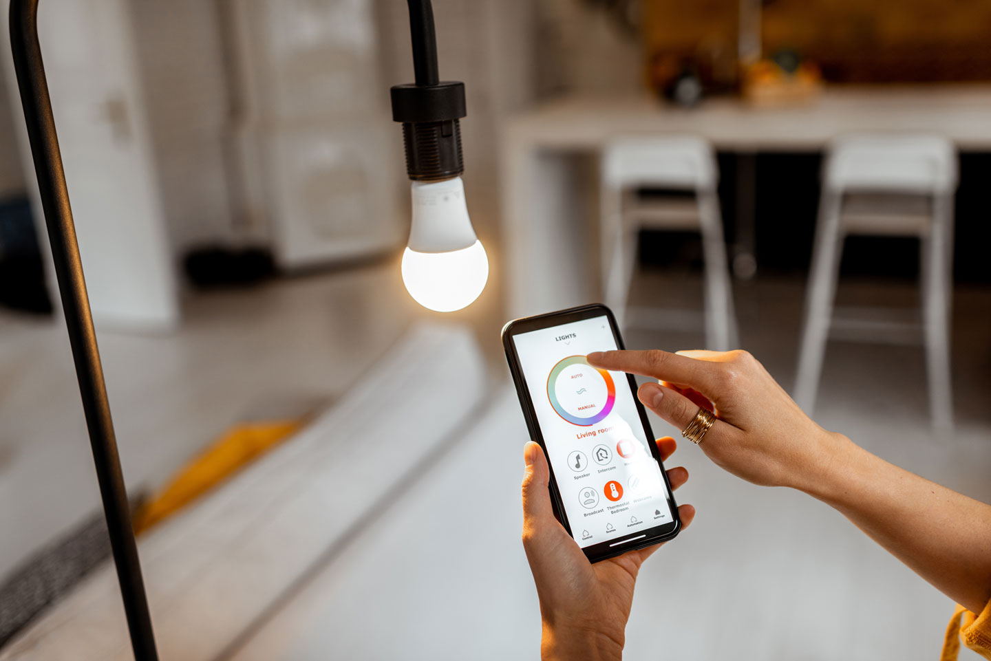Person adjusting color settings of a smart light bulb using a smartphone app in a modern living room.
